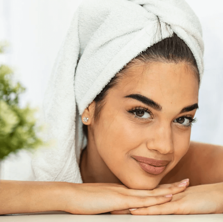 Woman with a towel on her head enjoying skincare routine with Ultra Relief Roller for a radiant appearance.