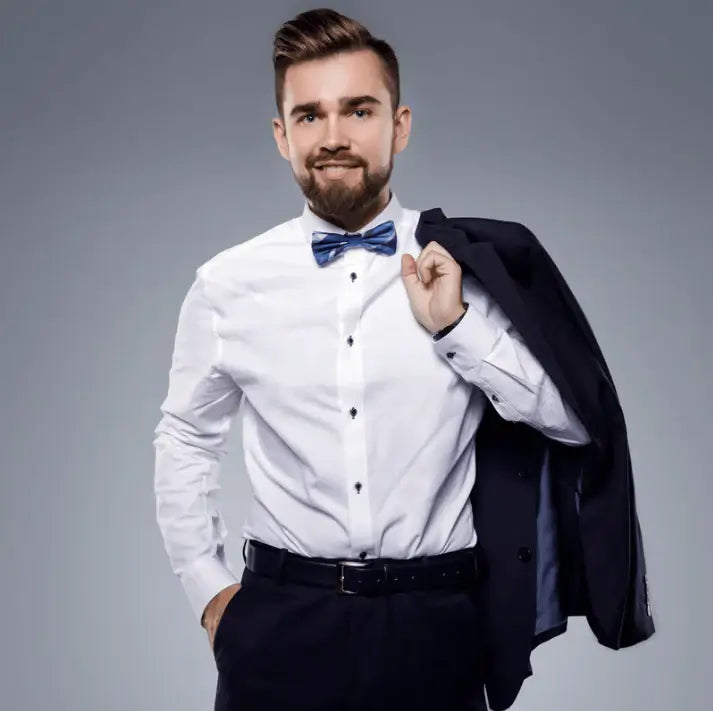 Young man in a white shirt and bow tie holding a black suit jacket on a gray background.
