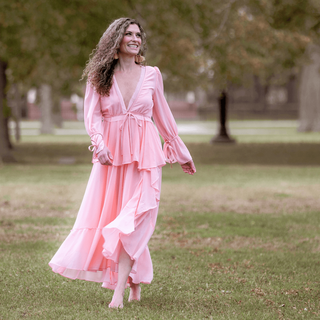 Woman in a flowy pink dress walking in a park, showcasing elegance and natural beauty.