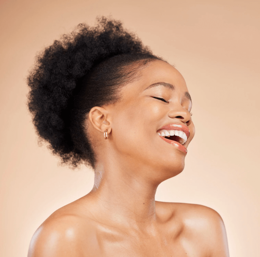 A smiling woman with natural hair and glowing skin, embodying beauty and joy in her personal routine.