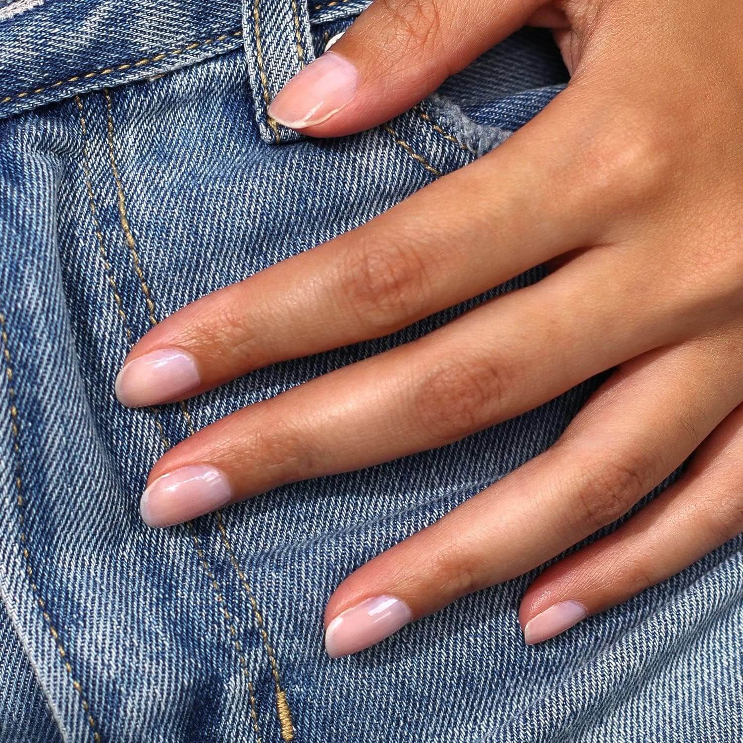 Close-up of a hand with elegant, natural nails resting on denim fabric.