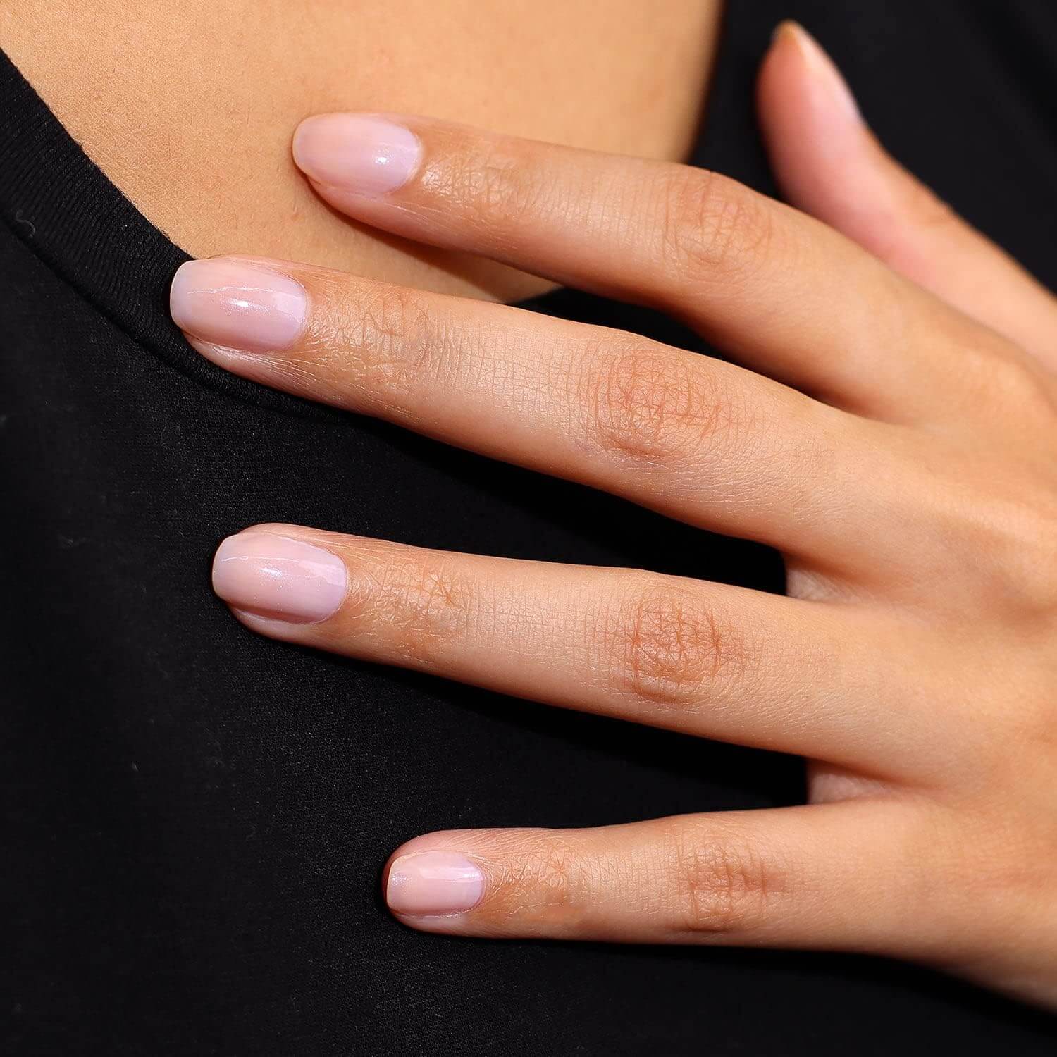 Close-up of a hand with natural-looking, light pink nails resting on a black top.