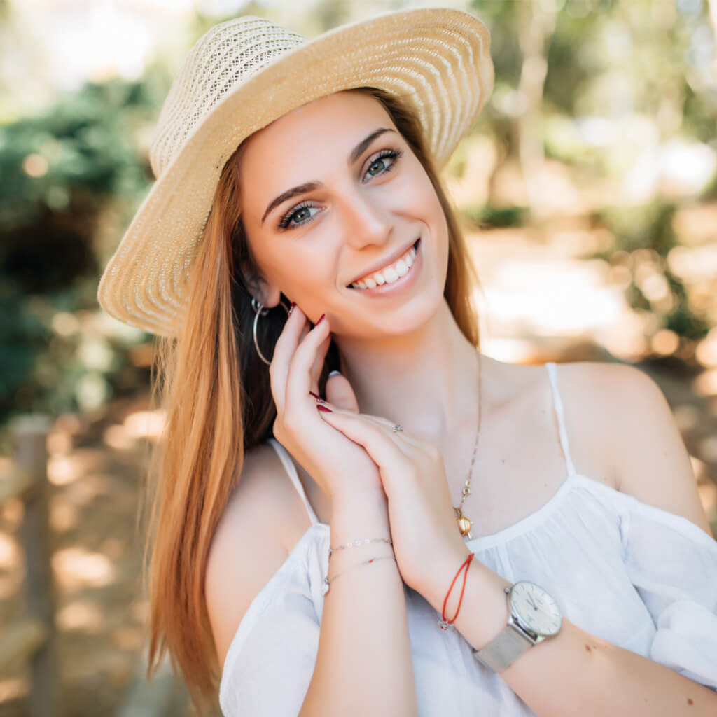 Portrait of a smiling woman in a sun hat showcasing natural beauty in a sunny outdoor setting.