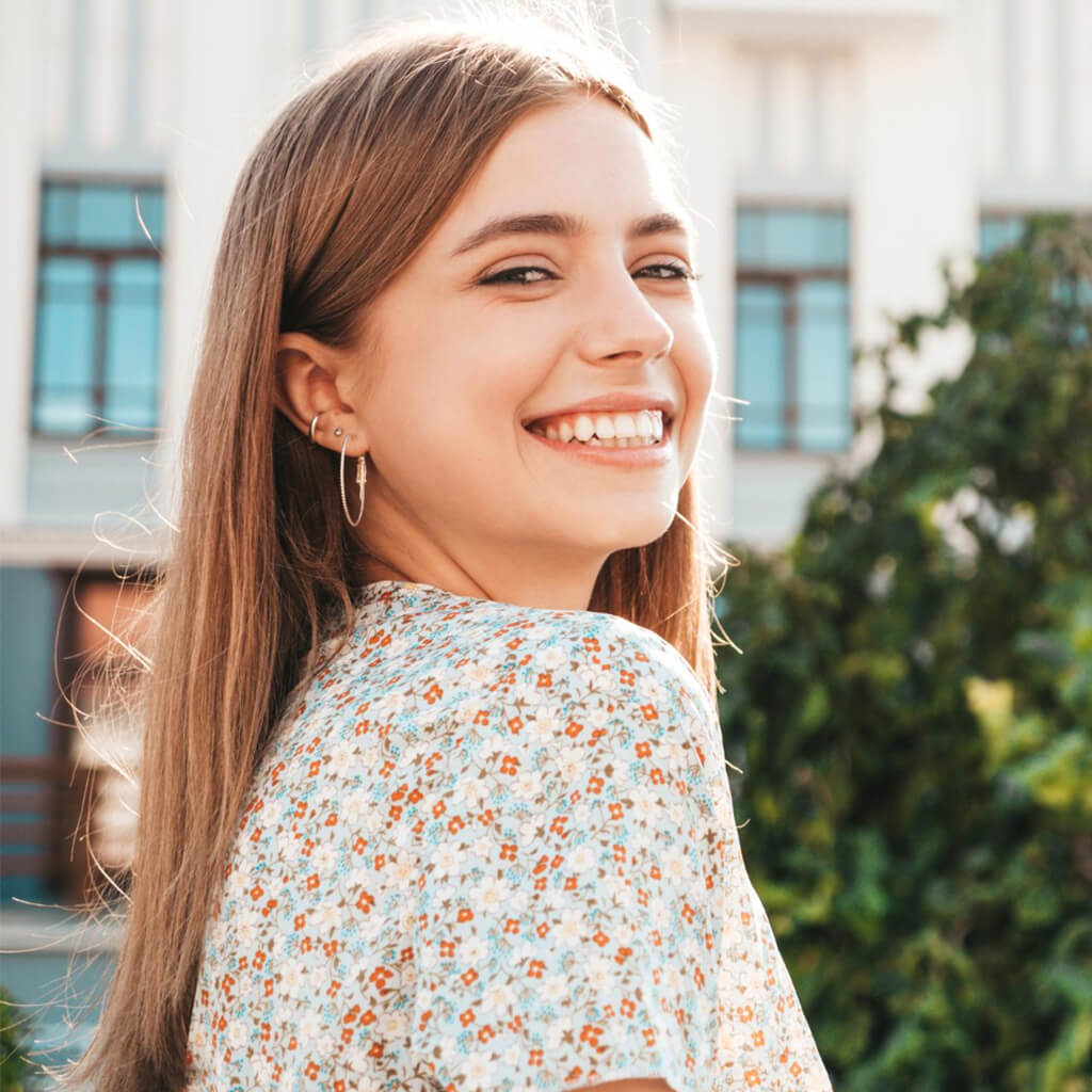 Young woman smiling in a floral dress, showcasing a radiant and joyful expression outdoors.